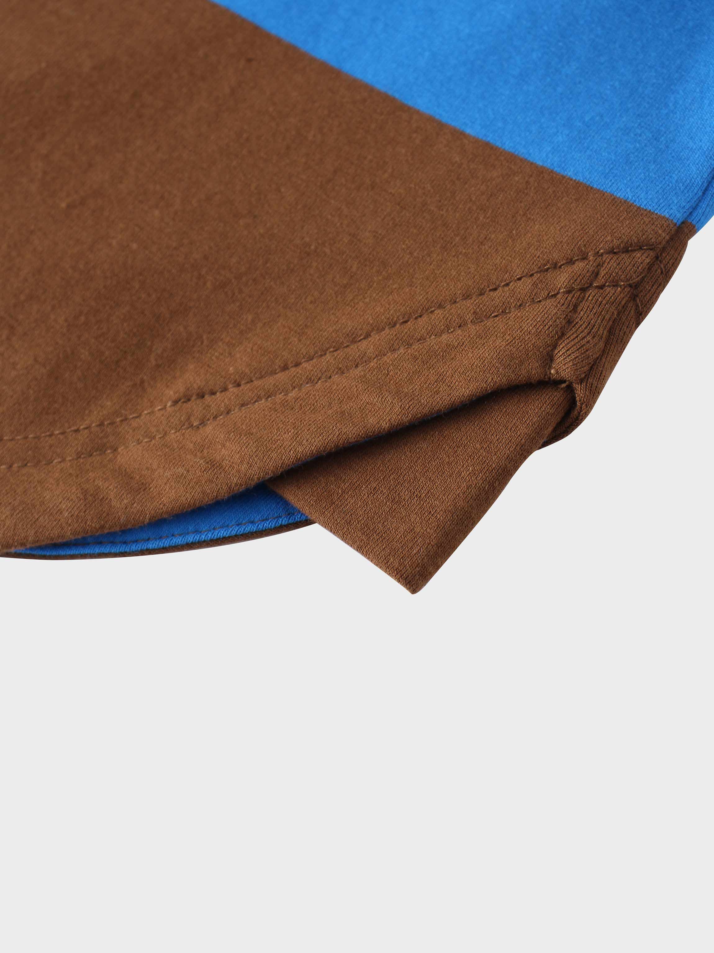 A close-up of the bottom hem of the color-blocked garment. The image shows the neat, double-stitched seam on the brown fabric, with the blue fabric visible on the reverse side.
