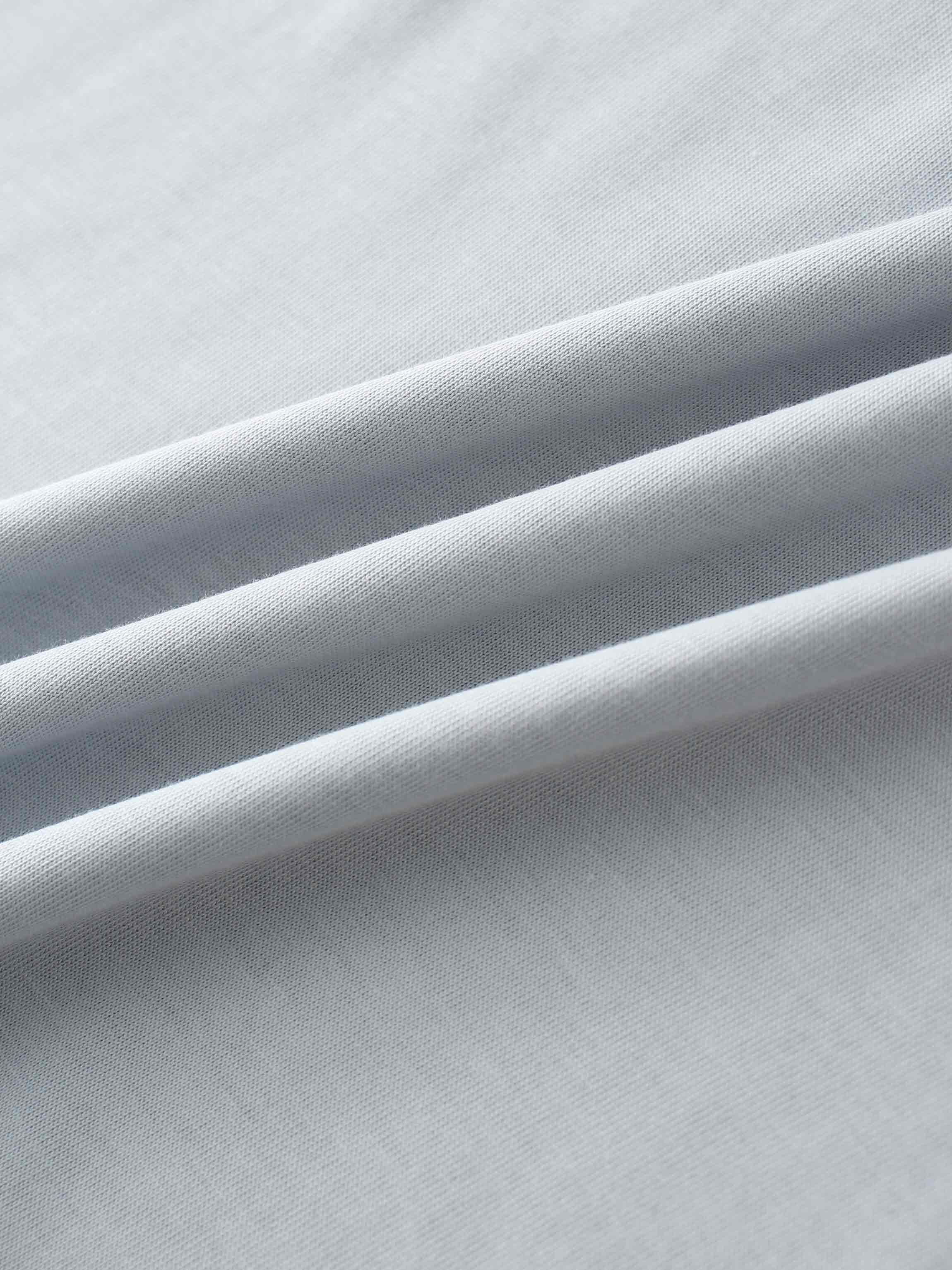 A close-up of the smooth, light gray fabric. The material is gathered into several soft, diagonal folds that catch the light.