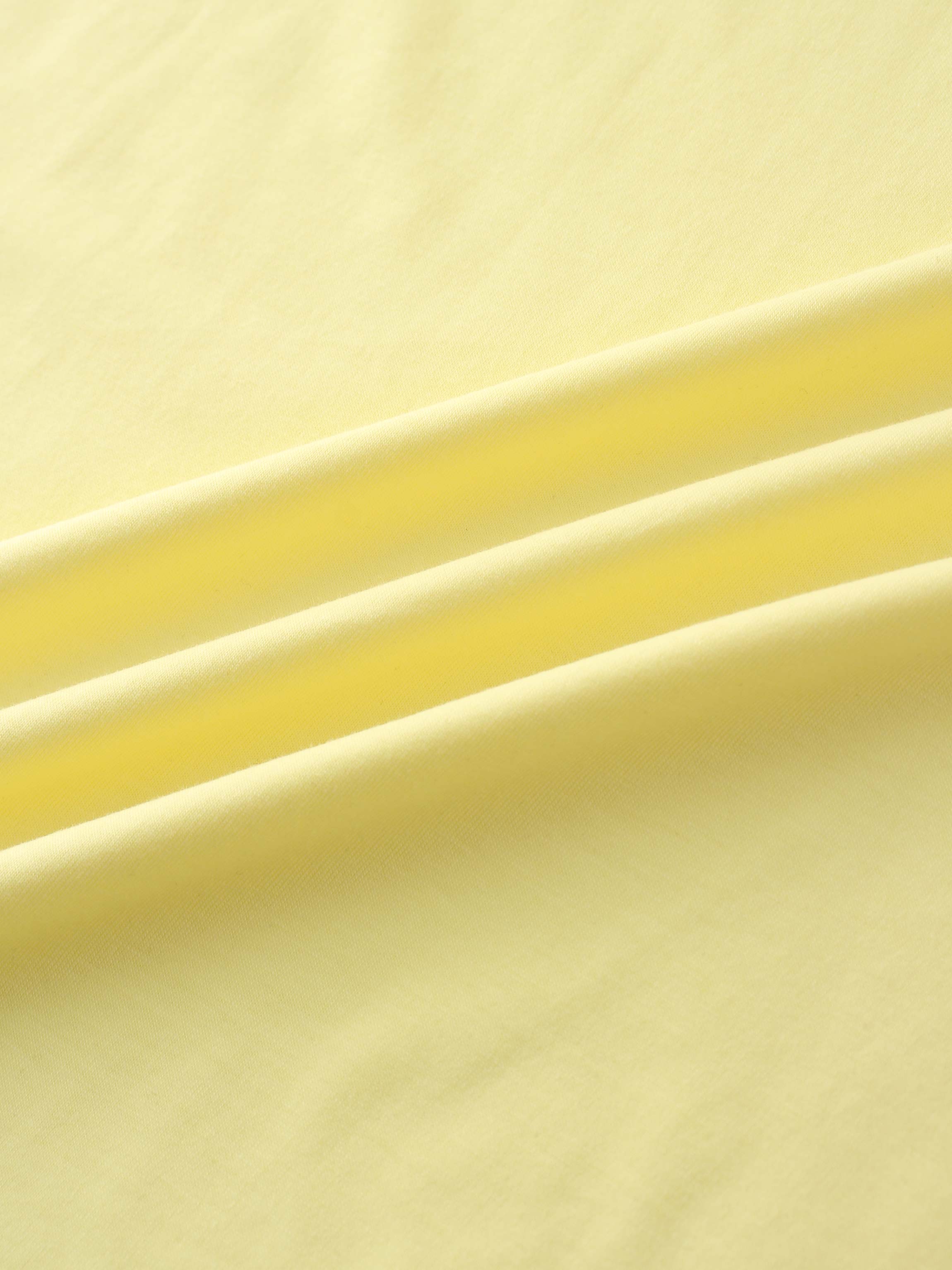 A close-up of a smooth fabric in a pale yellow color. The material is arranged in several soft, diagonal folds.