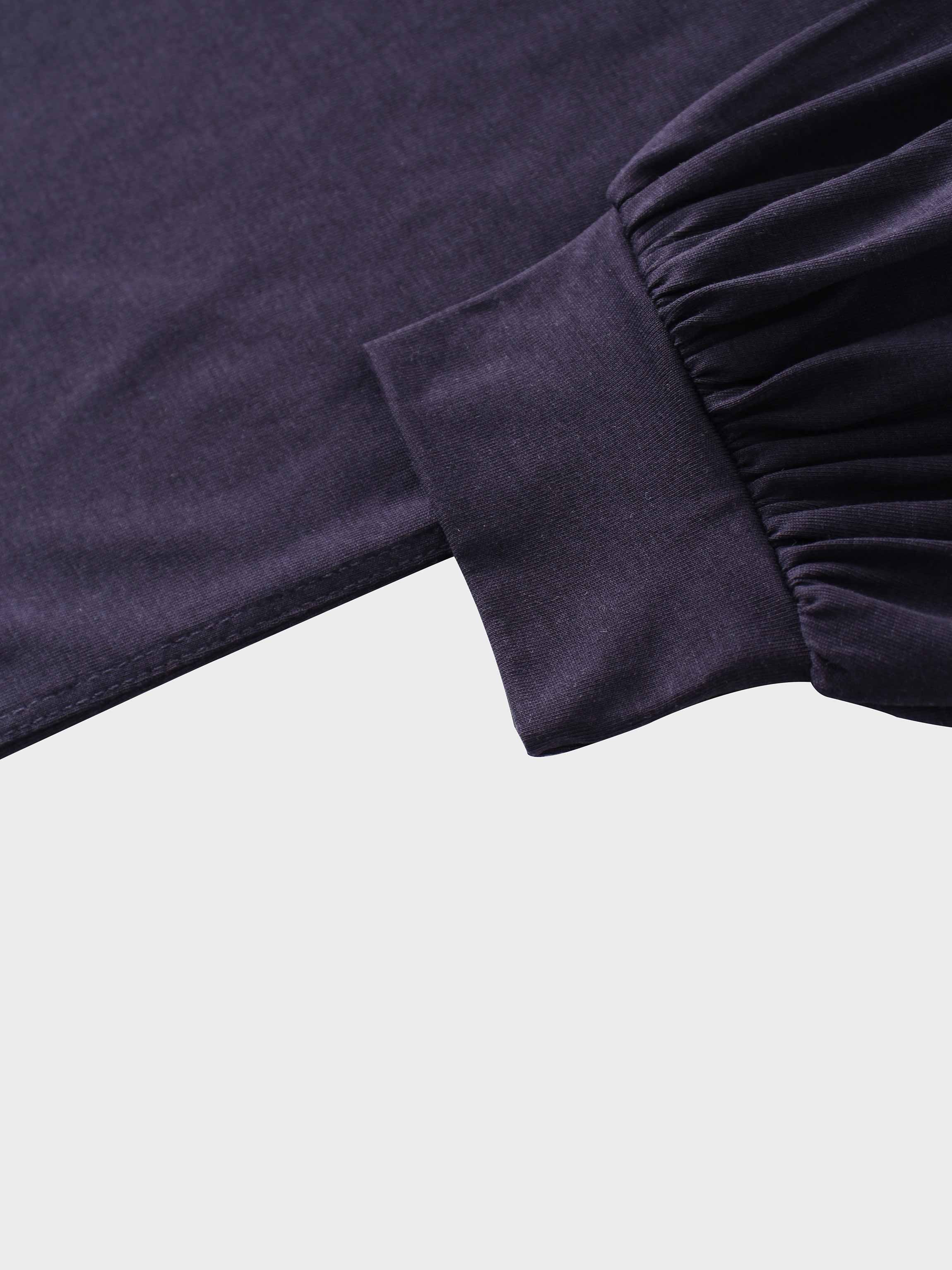 A close-up of the sleeve of the dark purple garment. The main fabric is gathered where it attaches to a wide, smooth cuff at the wrist.