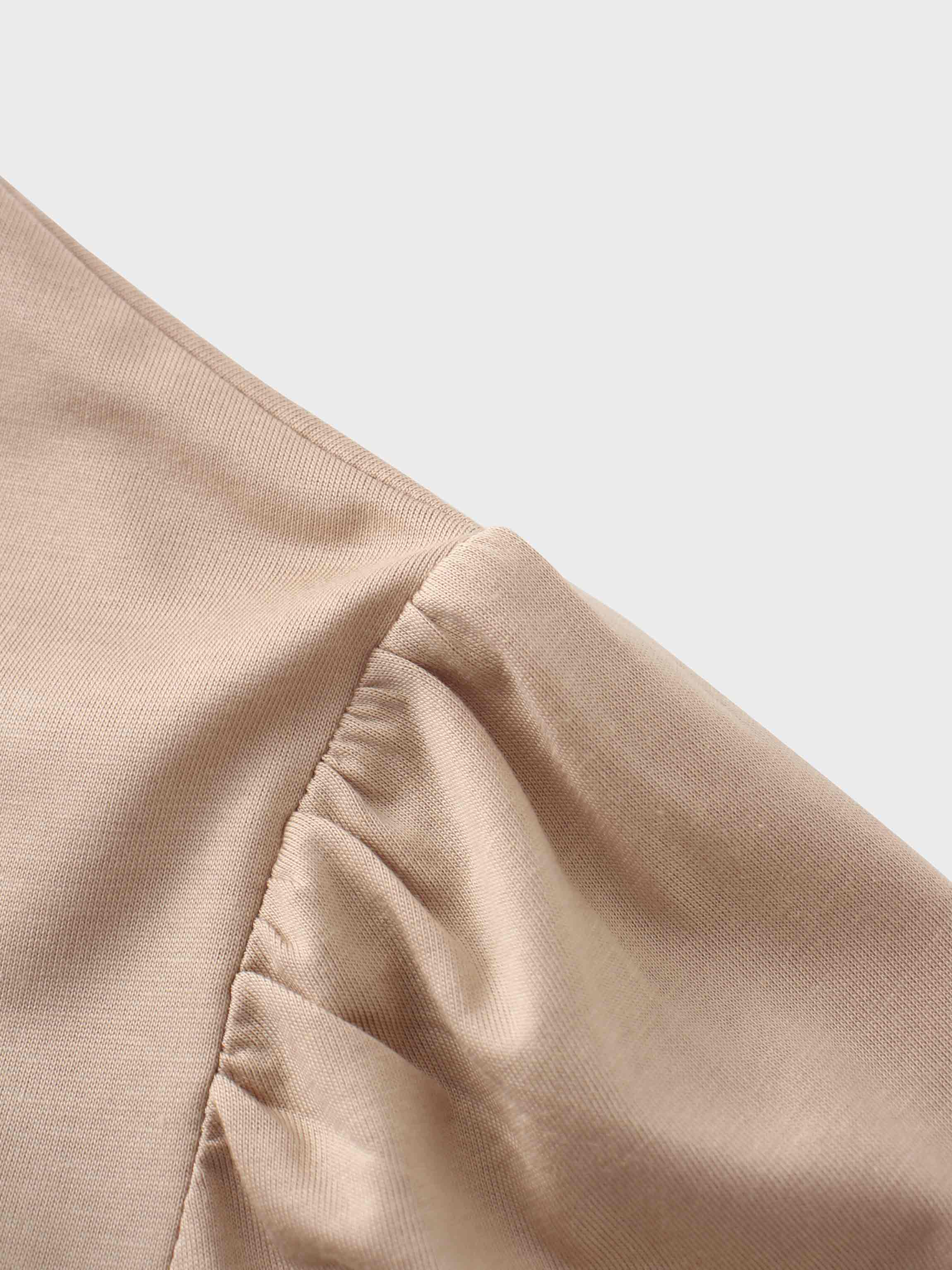 A close-up of the shoulder seam on the beige garment. The fabric at the top of the sleeve is gathered, creating a slight puff effect where it joins the body of the shirt.