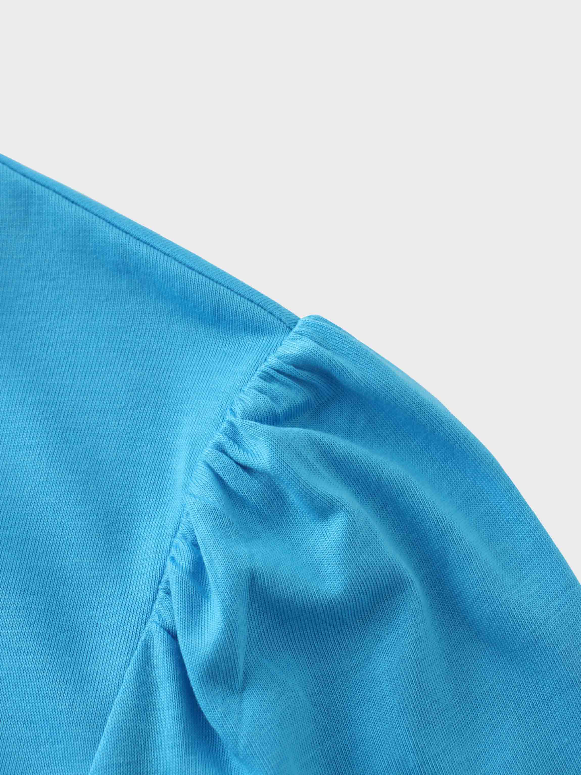 A close-up of the shoulder of the bright blue shirt. The fabric at the top of the sleeve is gathered at the seam, creating a puffed shoulder detail.
