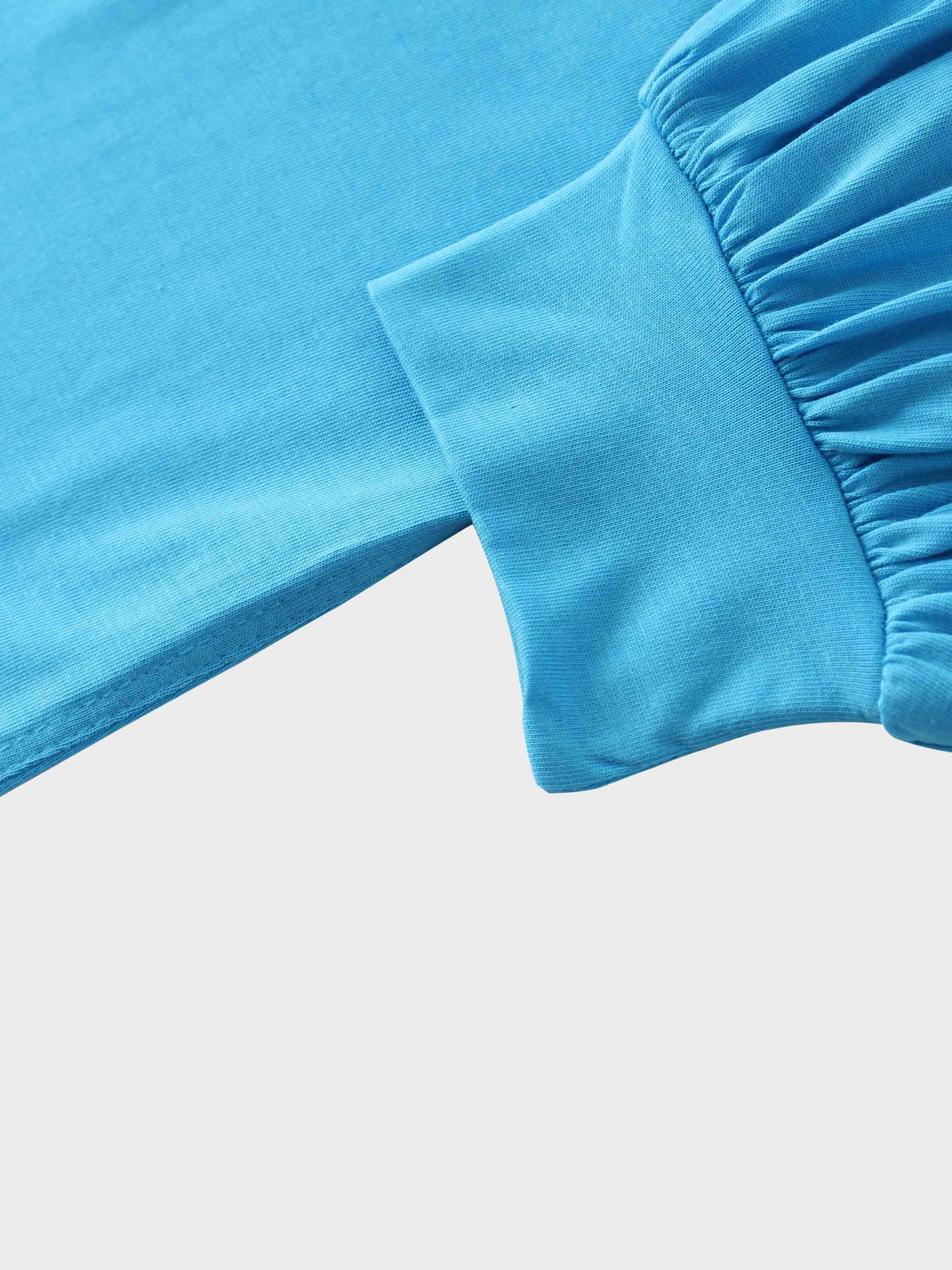 A close-up of the sleeve of the bright blue garment. The main fabric is gathered where it attaches to a wide, smooth cuff at the wrist.