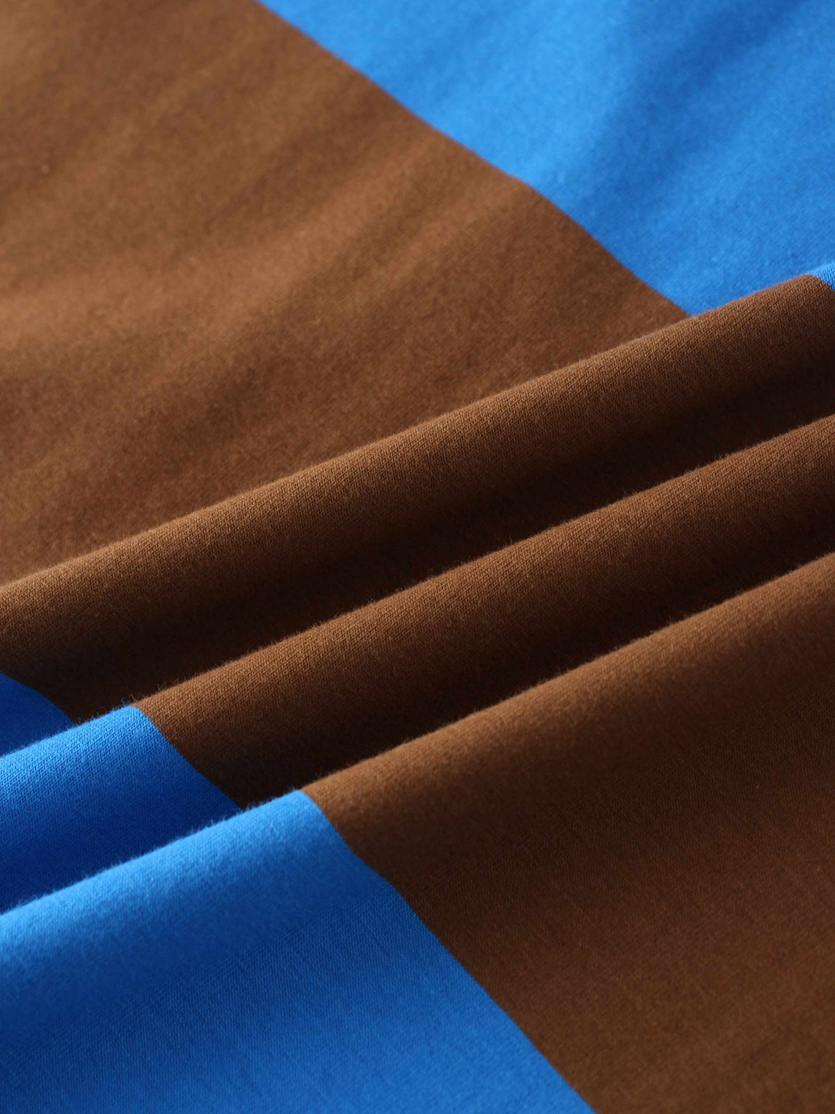 A close-up of a color-blocked fabric arranged in soft folds. The smooth material features wide panels of rich brown and vibrant blue.