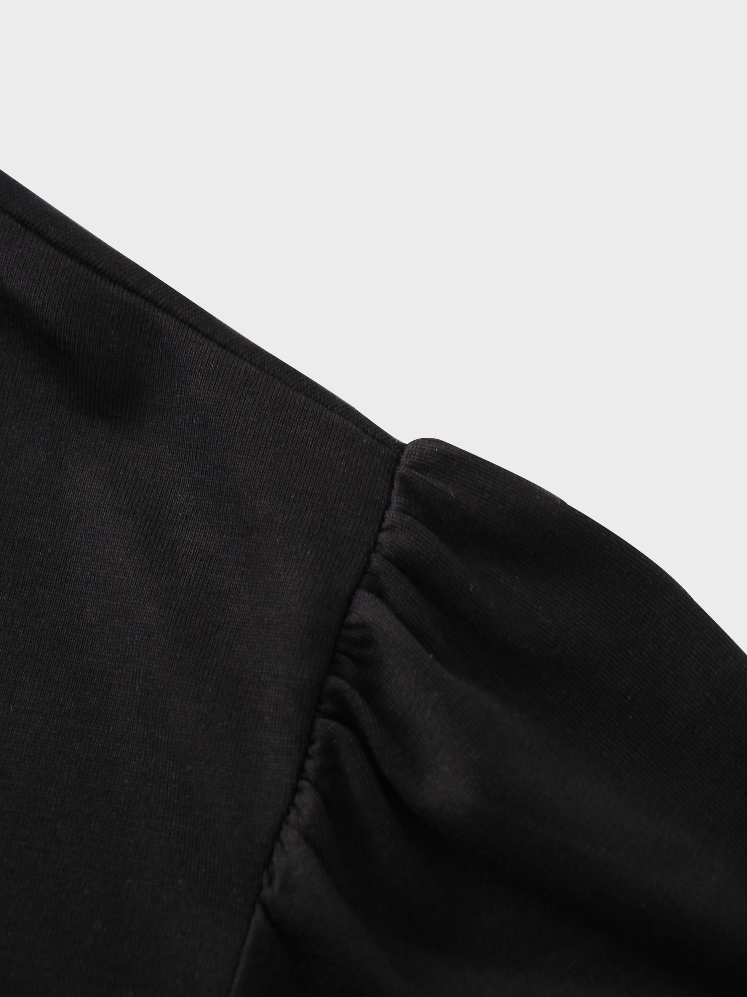 A close-up of the shoulder of the black shirt. The fabric at the top of the sleeve is gathered where it is sewn into the shoulder, creating a puff sleeve detail.