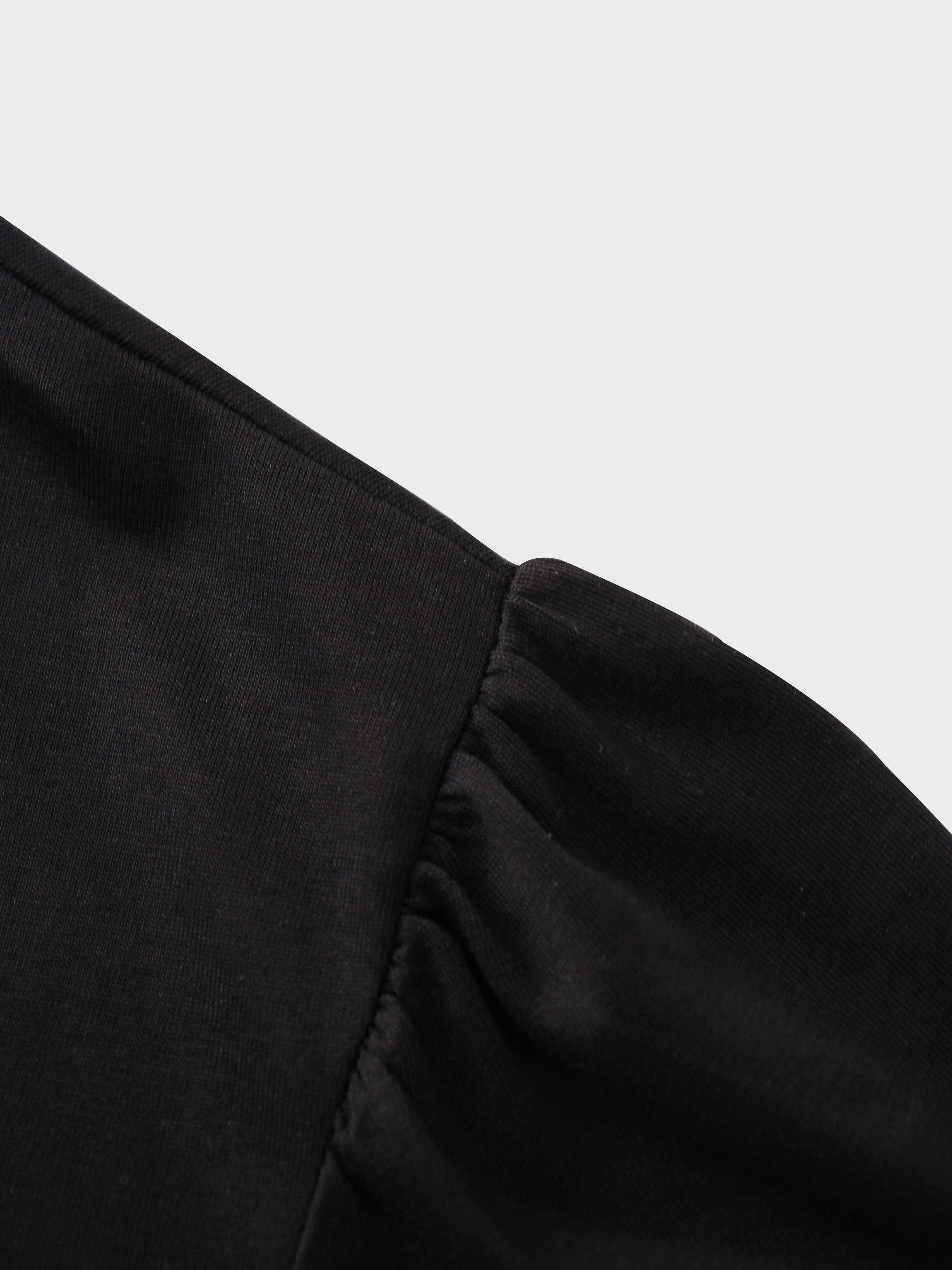 A close-up of the shoulder of the black shirt. The fabric at the top of the sleeve is gathered where it is sewn into the shoulder, creating a puff sleeve detail.