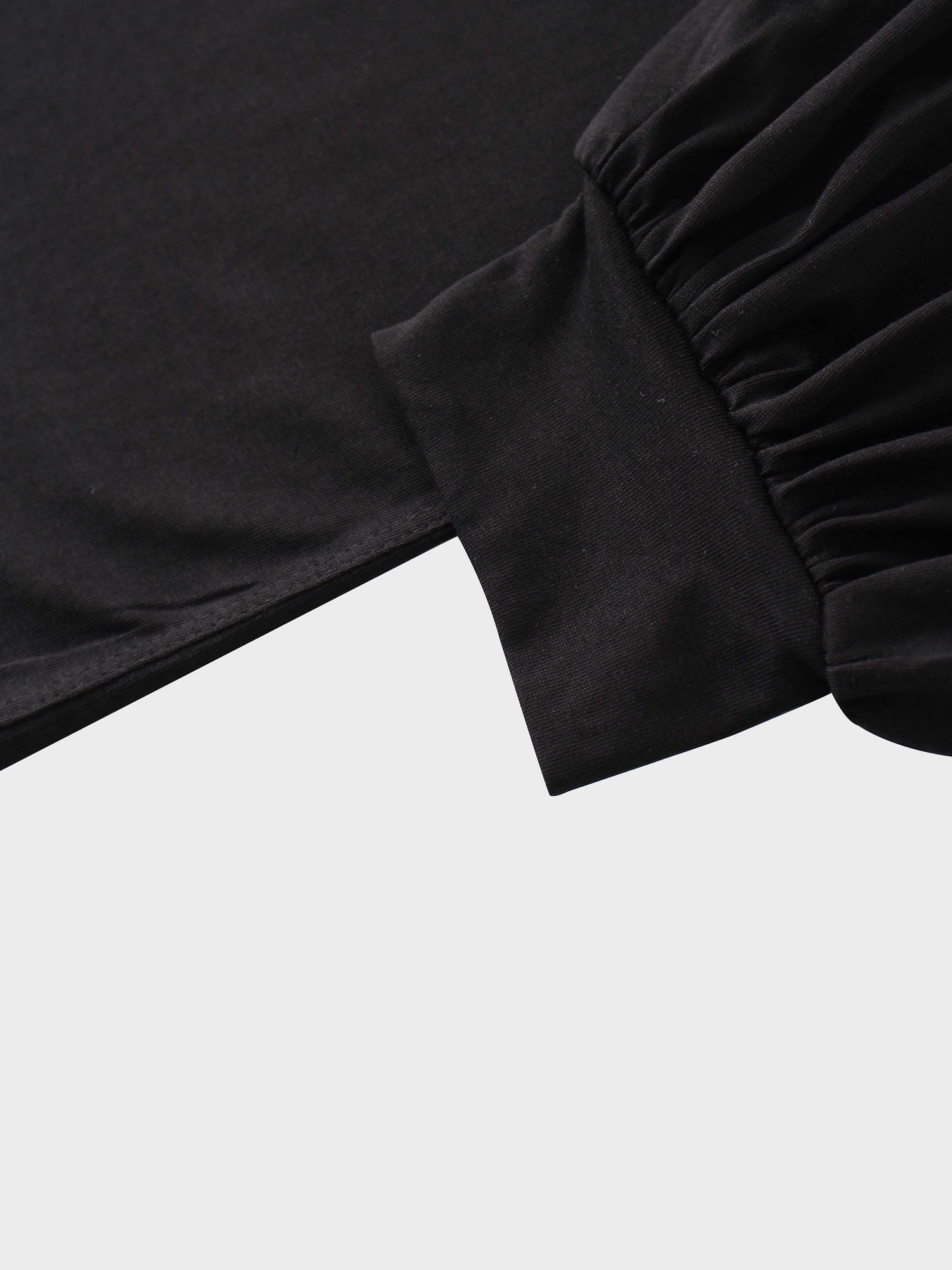 A close-up of the sleeve of the black garment. The main fabric is gathered where it attaches to a wide, smooth cuff at the wrist.