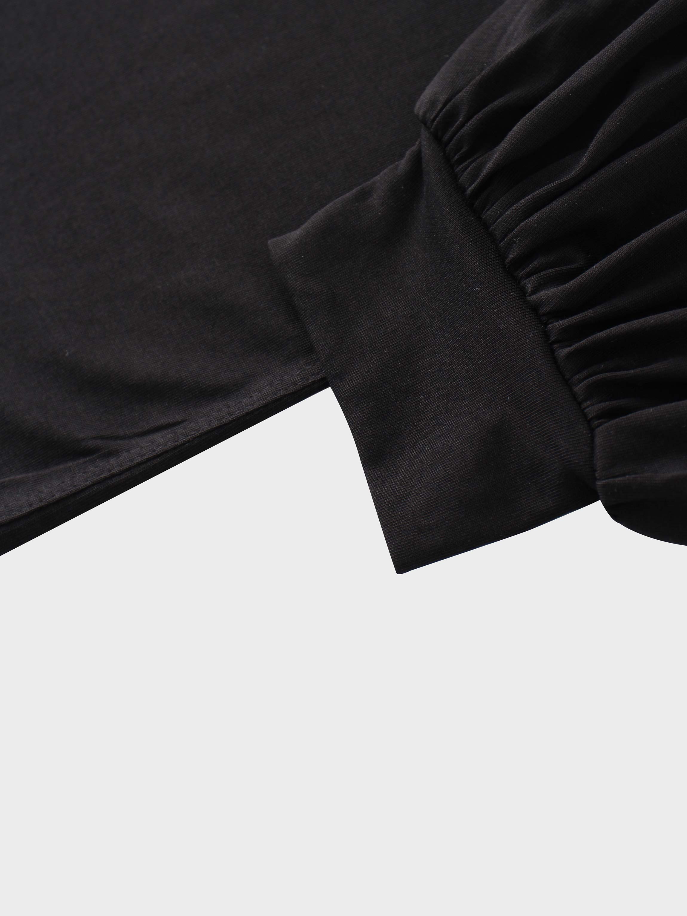 A close-up of the sleeve of the black garment. The main fabric is gathered where it attaches to a wide, smooth cuff at the wrist.