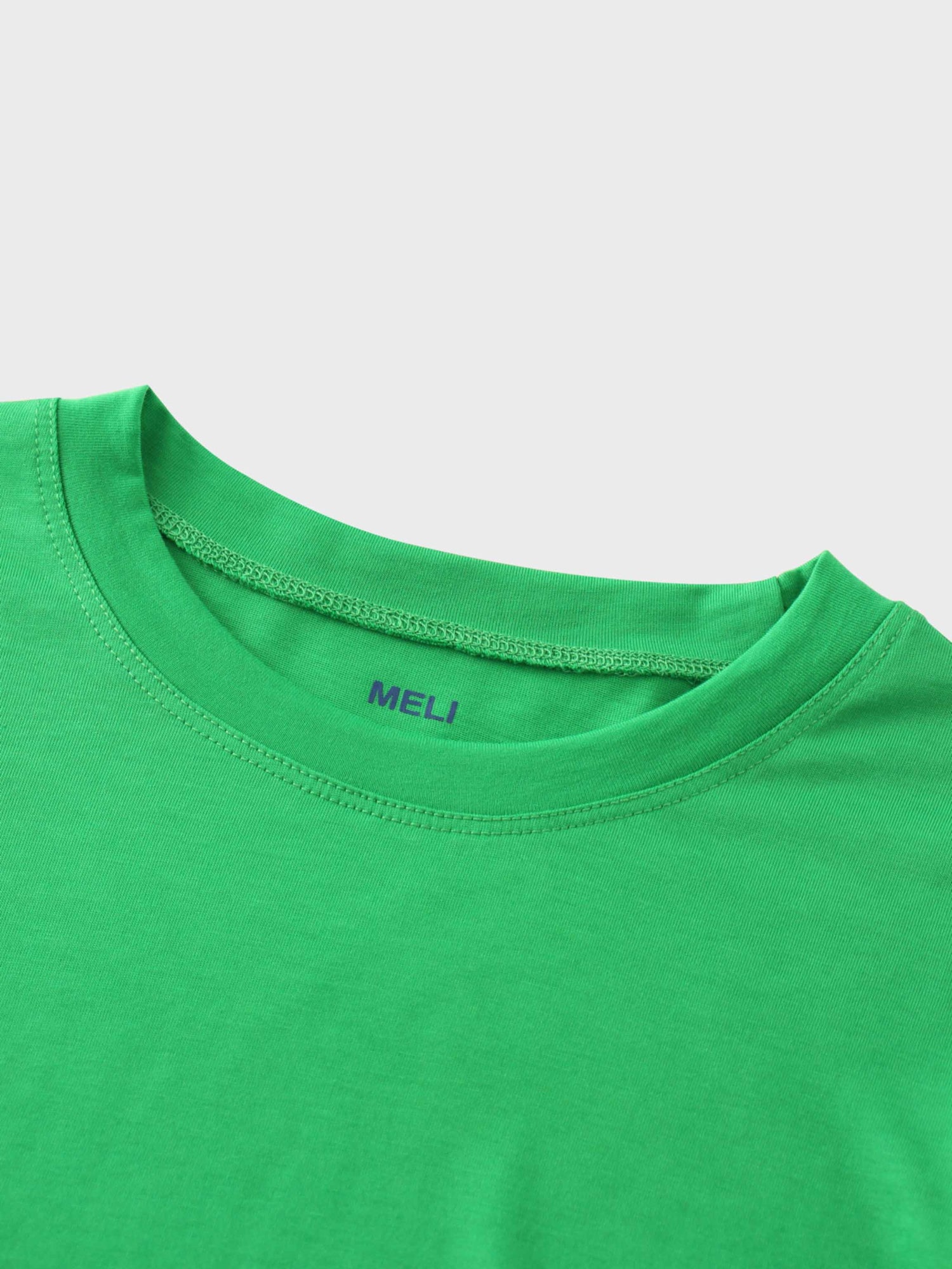 A close-up of the crewneck collar of the vibrant green t-shirt. On the inside, the brand name &quot;MELI&quot; is printed directly onto the fabric in blue.