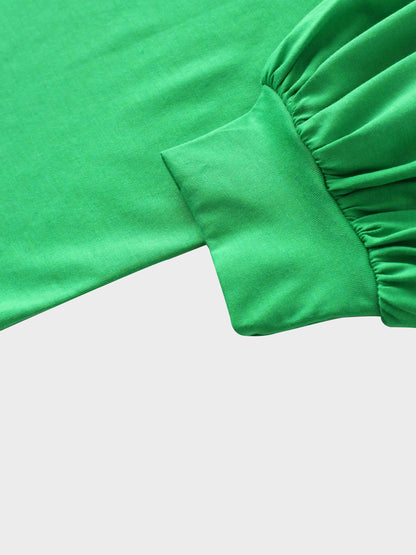 A close-up of the sleeve of the vibrant green garment. The main fabric is gathered where it attaches to a wide, smooth cuff at the wrist.
