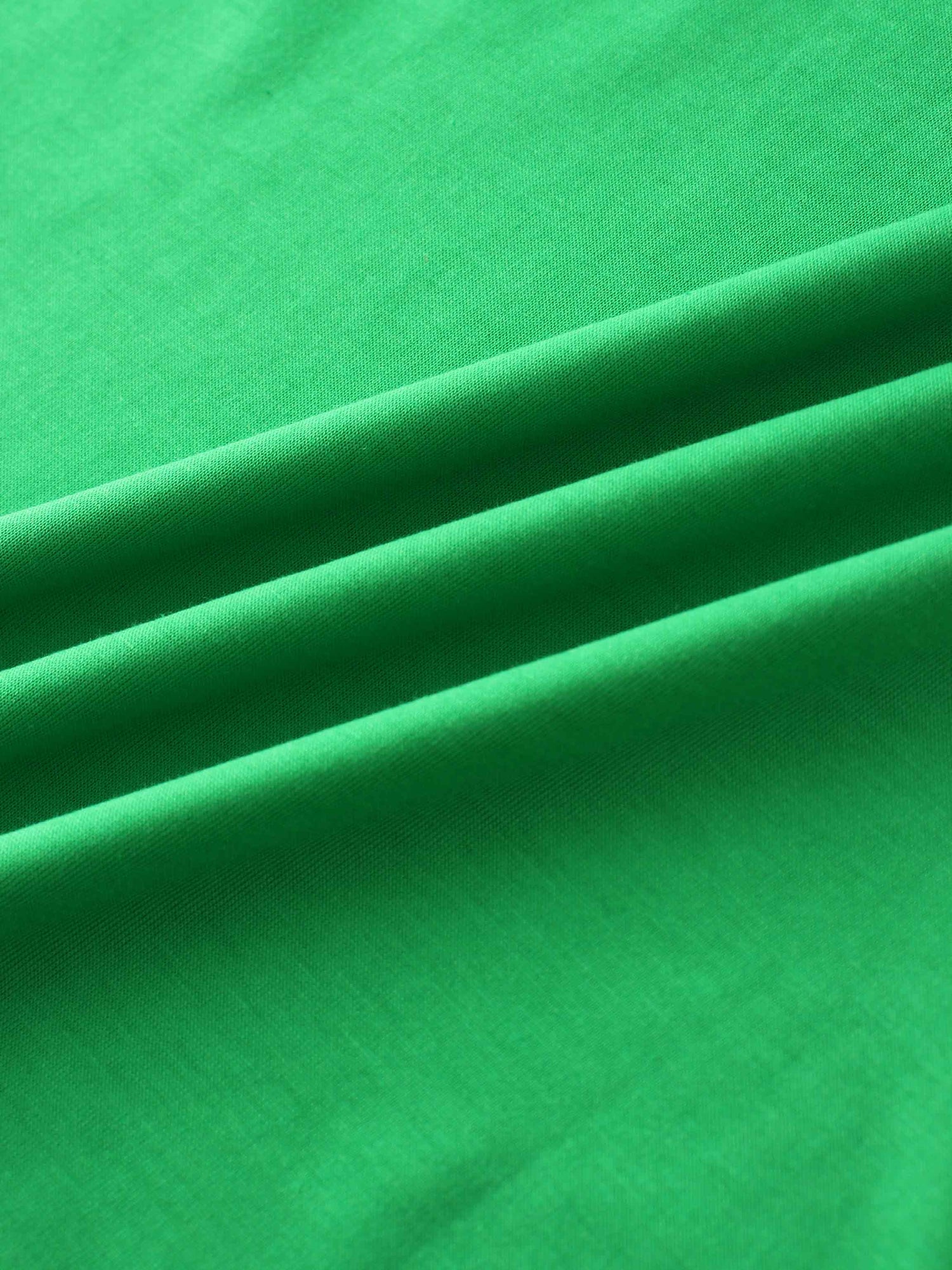 A close-up of a smooth fabric in a vibrant green color. The material is arranged in several soft, diagonal folds.