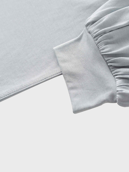 A close-up of the sleeve of the light gray garment, showing how the main fabric is gathered where it attaches to a wide, smooth cuff at the wrist.
