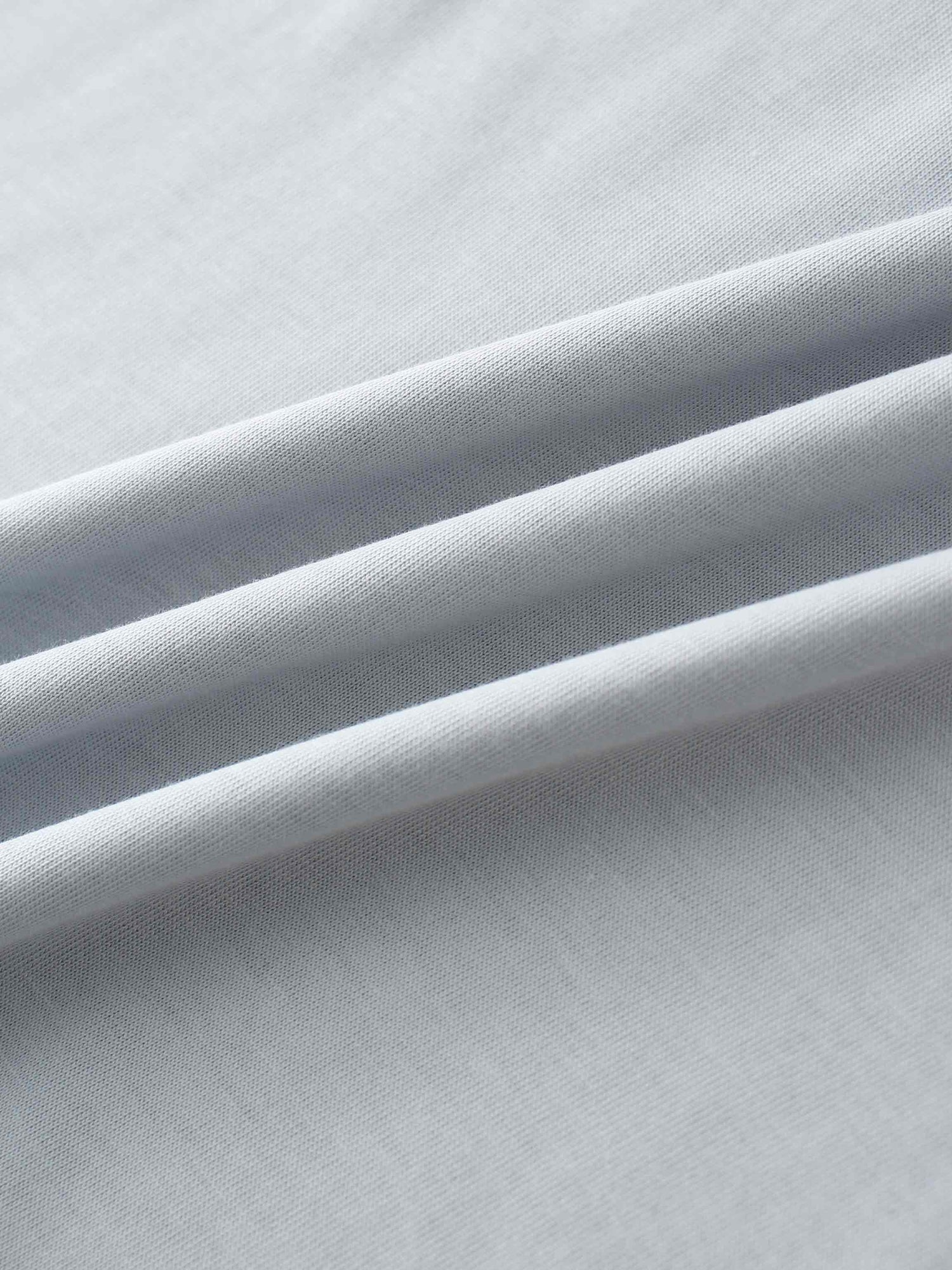 A close-up of the smooth, light gray fabric. The material is gathered into several soft, diagonal folds that catch the light.