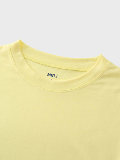 A close-up of the crewneck collar of the pale yellow t-shirt. On the inside, the brand name "MELI" is printed directly onto the fabric in blue.