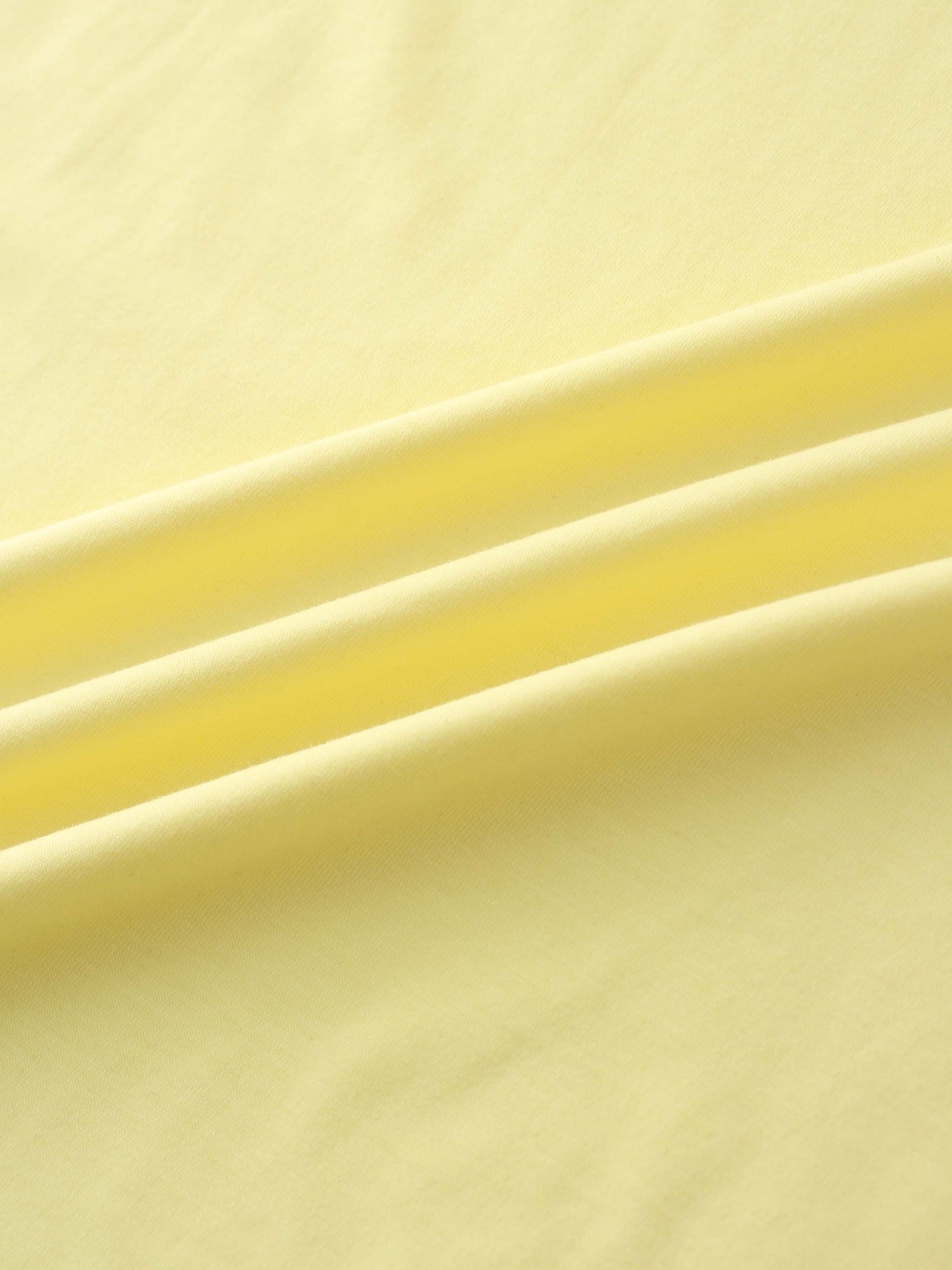 A close-up of a smooth fabric in a pale yellow color. The material is arranged in several soft, diagonal folds.