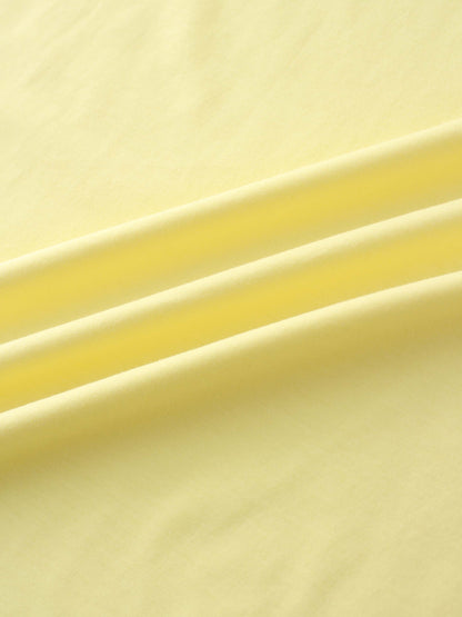 A close-up of a smooth fabric in a pale yellow color. The material is arranged in several soft, diagonal folds.