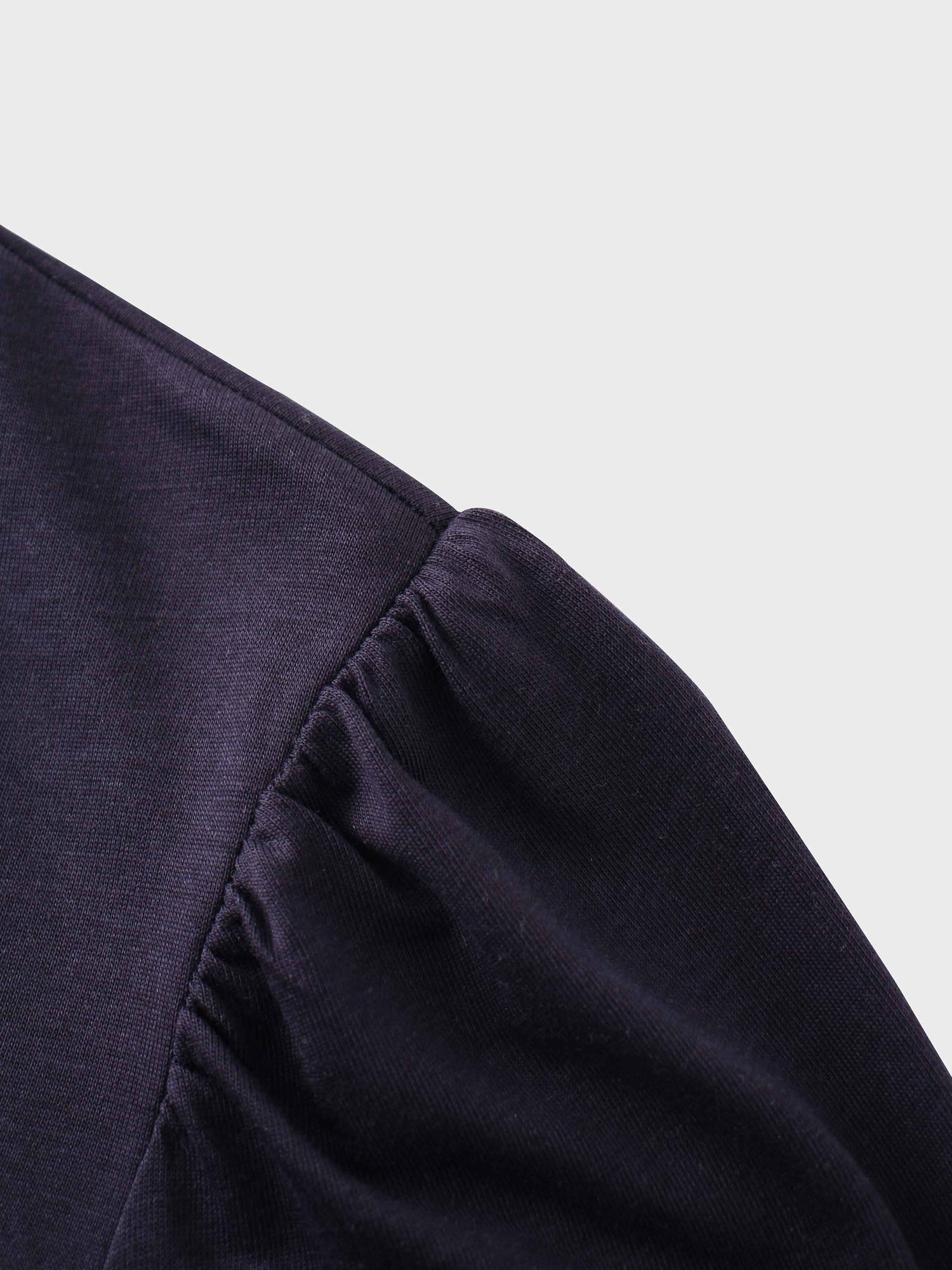 A close-up of the shoulder of the dark purple shirt. The fabric at the top of the sleeve is gathered where it is sewn into the shoulder, creating a puff sleeve detail.