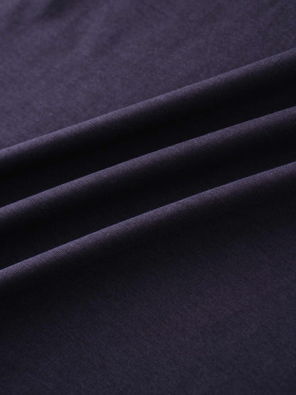 A close-up of a smooth fabric in a deep, dark purple color. The material is arranged in several soft, diagonal folds.