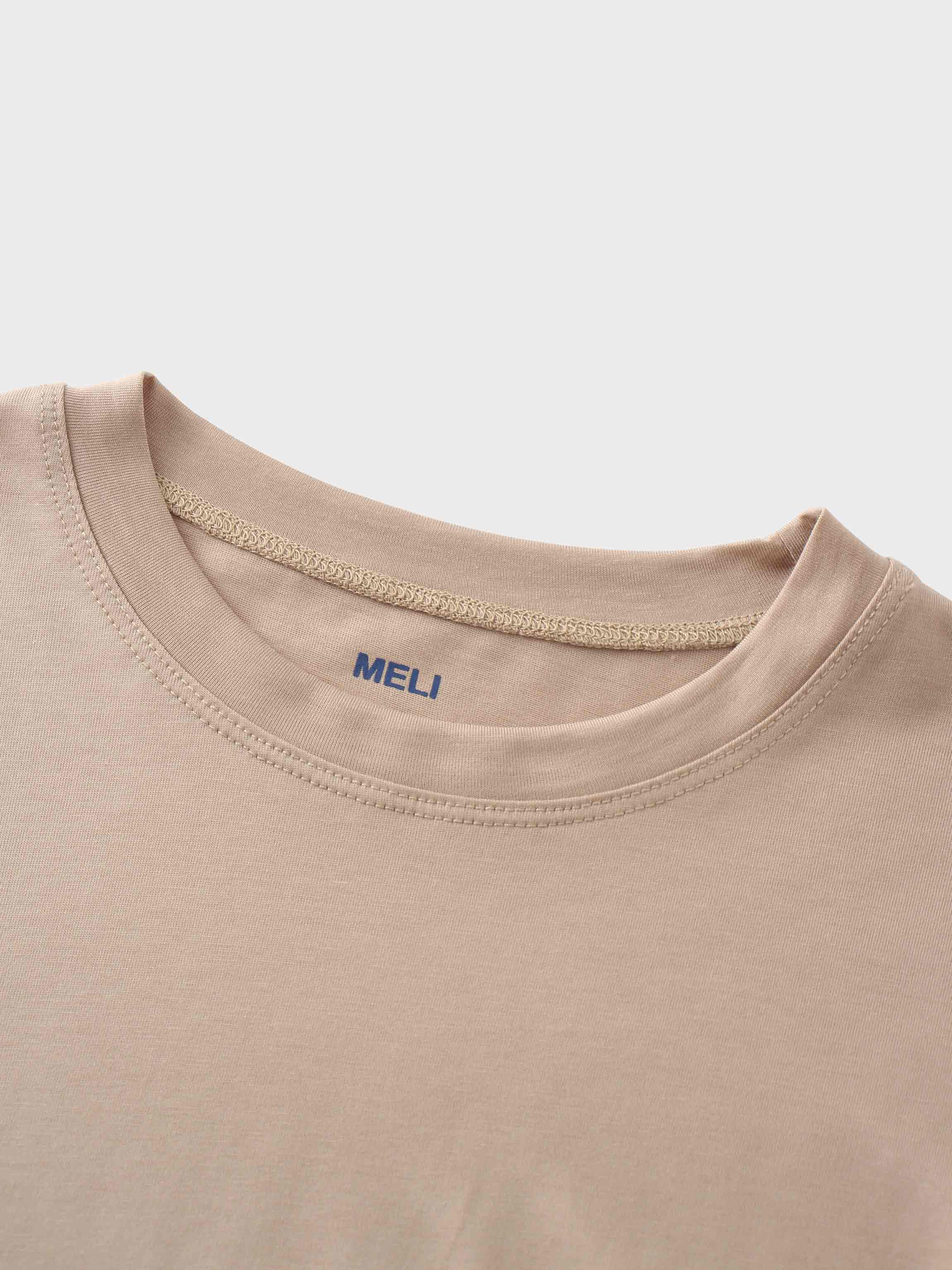 A close-up view of the crewneck collar on the beige t-shirt. The brand name &quot;MELI&quot; is printed in blue directly onto the fabric on the inside of the neck.