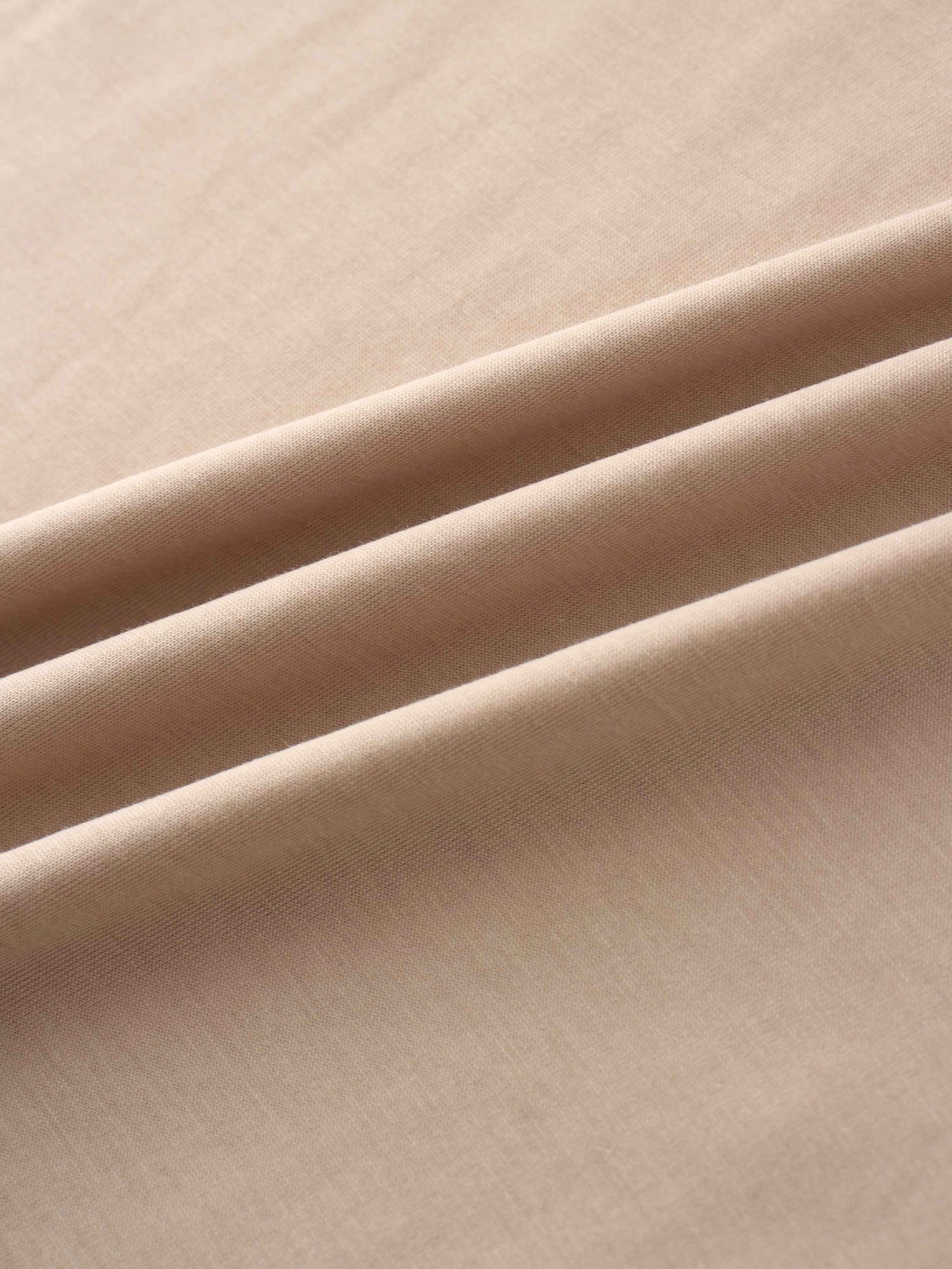 A close-up shot of the smooth, light-beige fabric. The material is arranged in several soft, diagonal folds that catch the light.