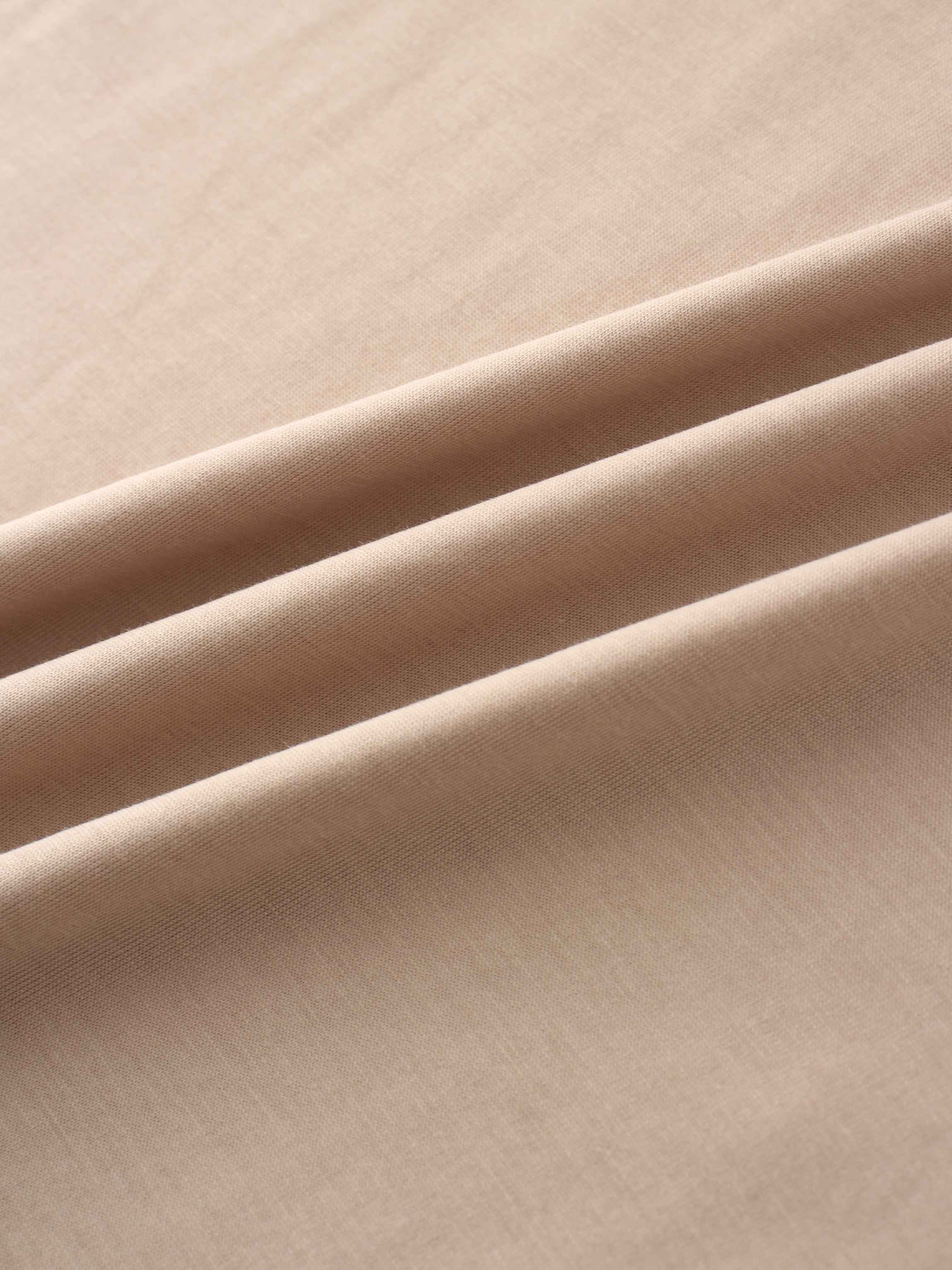 A close-up shot of the smooth, light-beige fabric. The material is arranged in several soft, diagonal folds that catch the light.