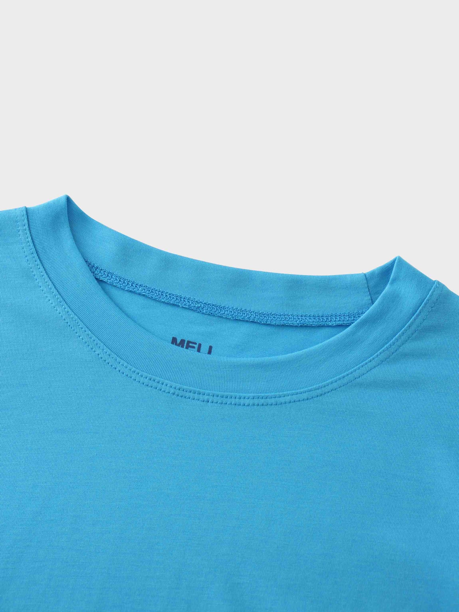 A close-up of the crewneck collar on the bright blue t-shirt. The brand name &quot;MELI&quot; is printed in a darker blue on the inside of the neck.