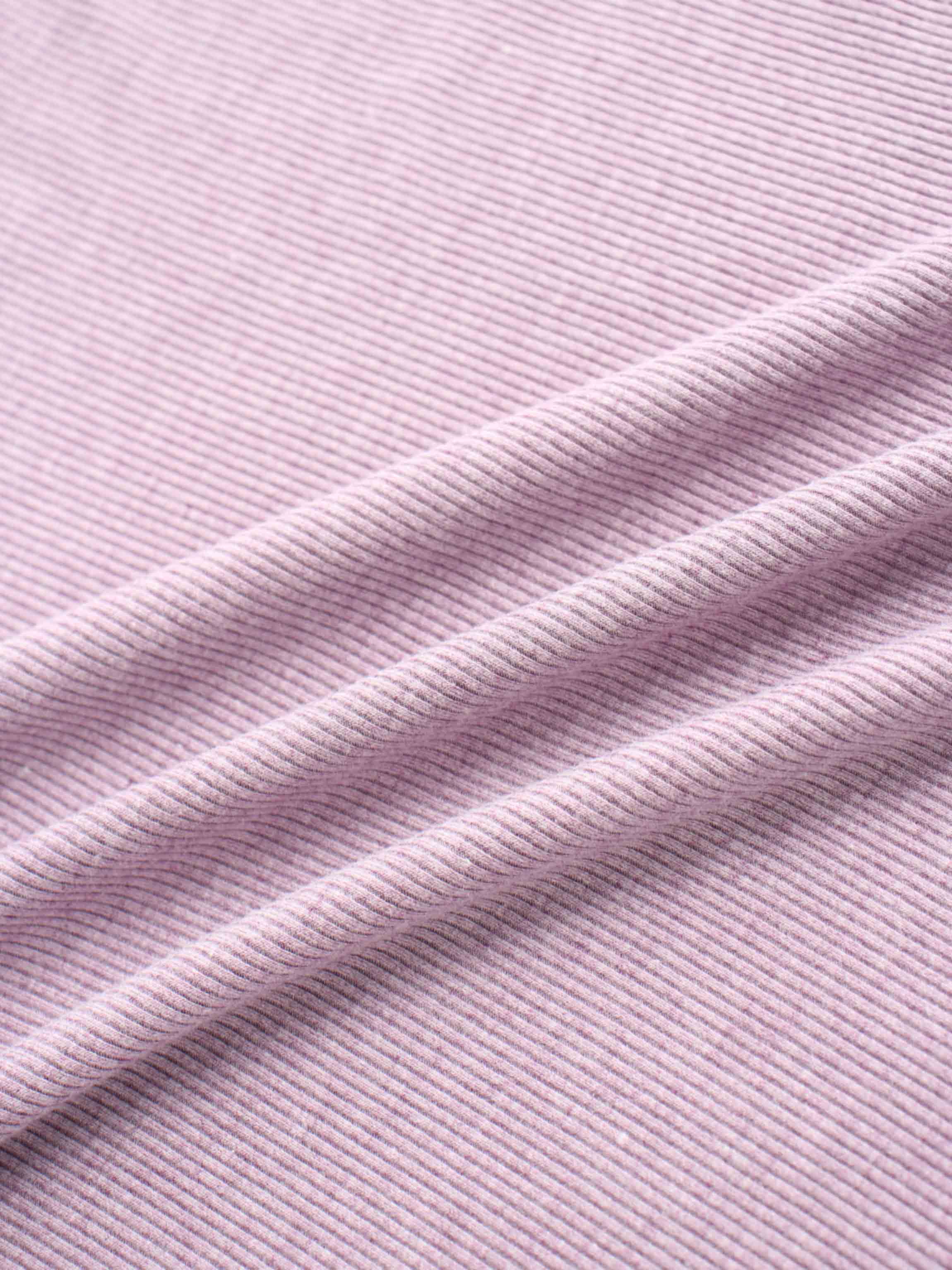 A soft, lavender-colored fabric with a finely ribbed texture. The material is folded, creating gentle diagonal lines and shadows.